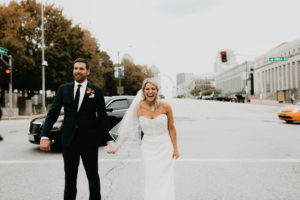 Bride and groom hold hands in crosswalk on street outside of St. Louis Union Station Hotel wedding.