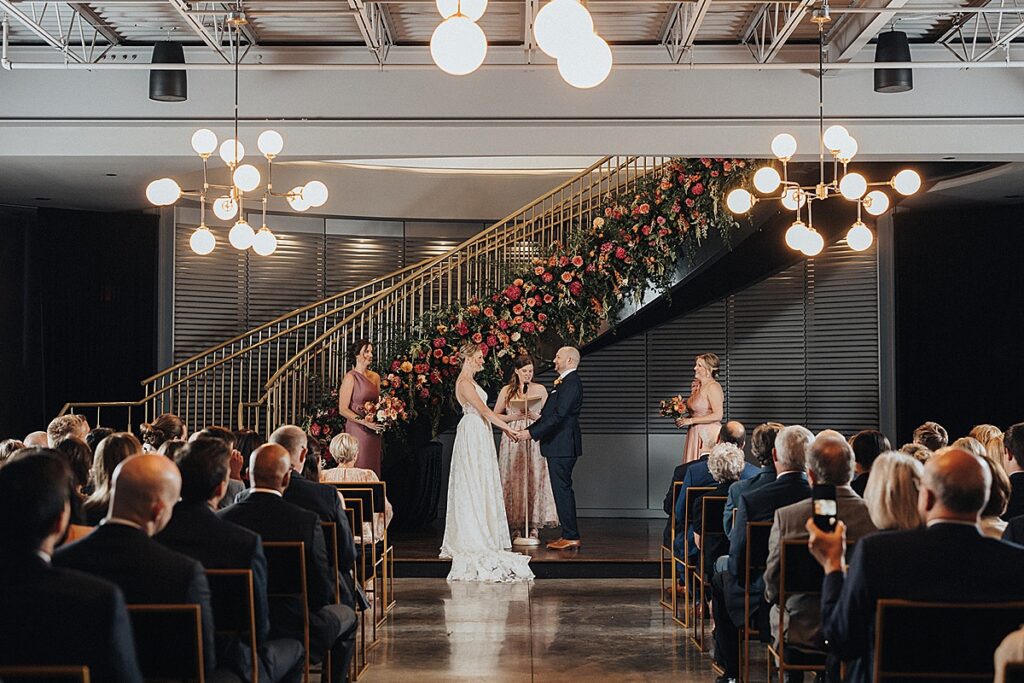 A bride and groom hand in hand during their ceremony inside at The Dogwood in the Grove in St. Louis, Missouri. 