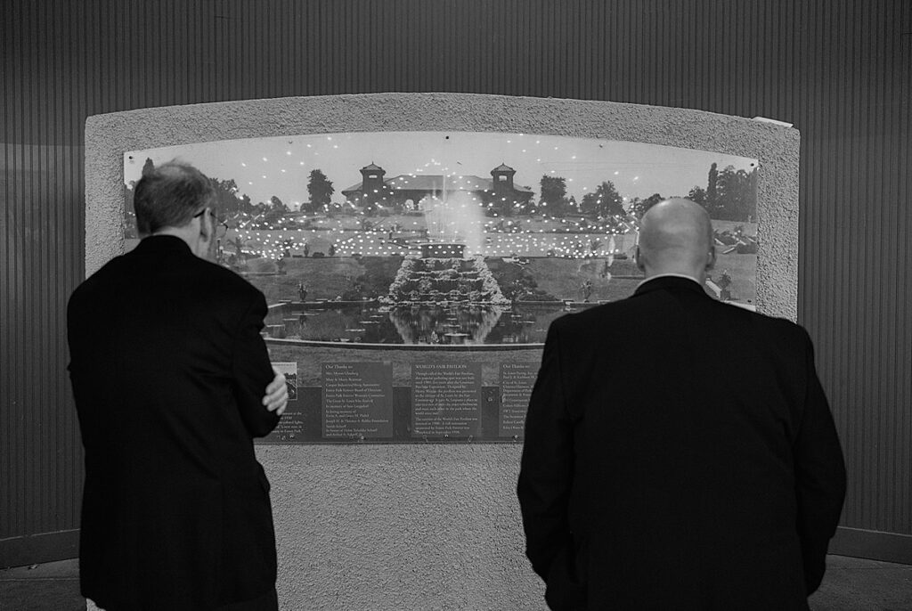 A black and white image of two men looking at a historic description of the World's Fair Pavilion in Forest Park.