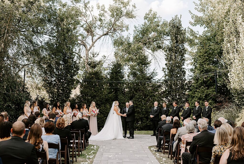 A bride and groom hand in hand getting married outdoors at Wild Carrot in St. Louis, Missouri.