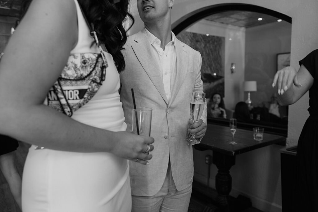 Black and white image of bride and groom looking at each other while drinking champagne.