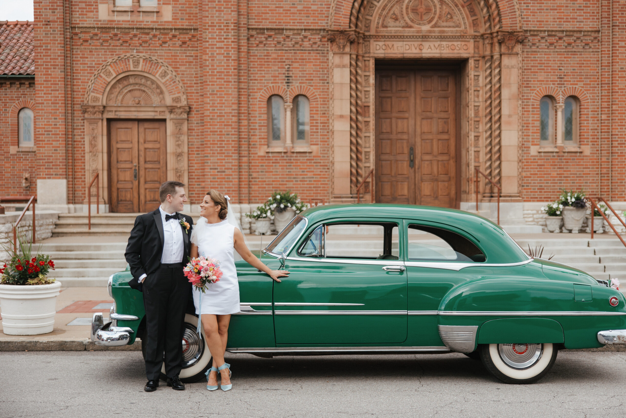 Bride wearing a retro 1960s short wedding dress and Groom in front of green vintage car at her Meet Me in St. Louis wedding