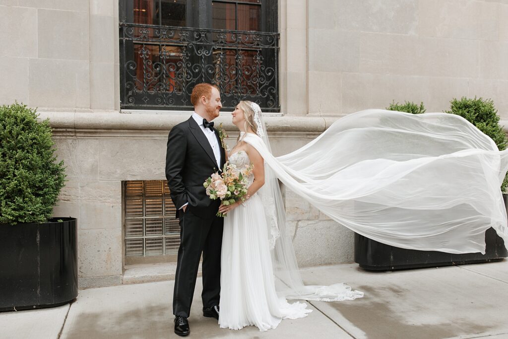 Bride and groom looking at each other while bridal cape is in the wind outside of the 21C Hotel in St. Louis, Missouri
