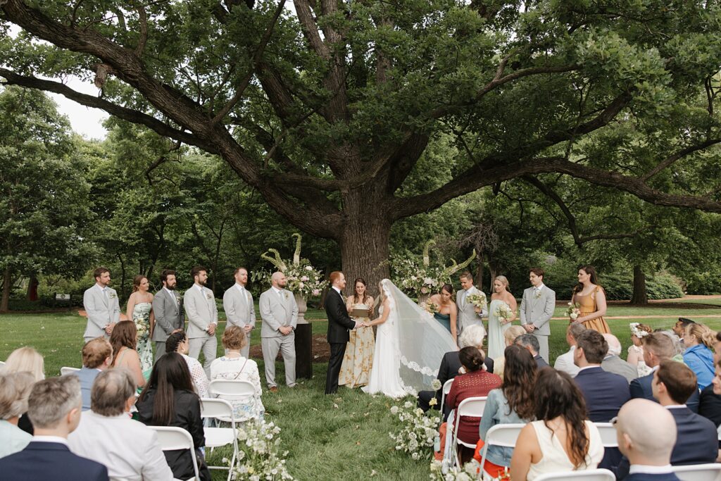 Bride and groom standing under large Oak tree during ceremony at Weddings on Magnolia in St. Louis, Missouri
