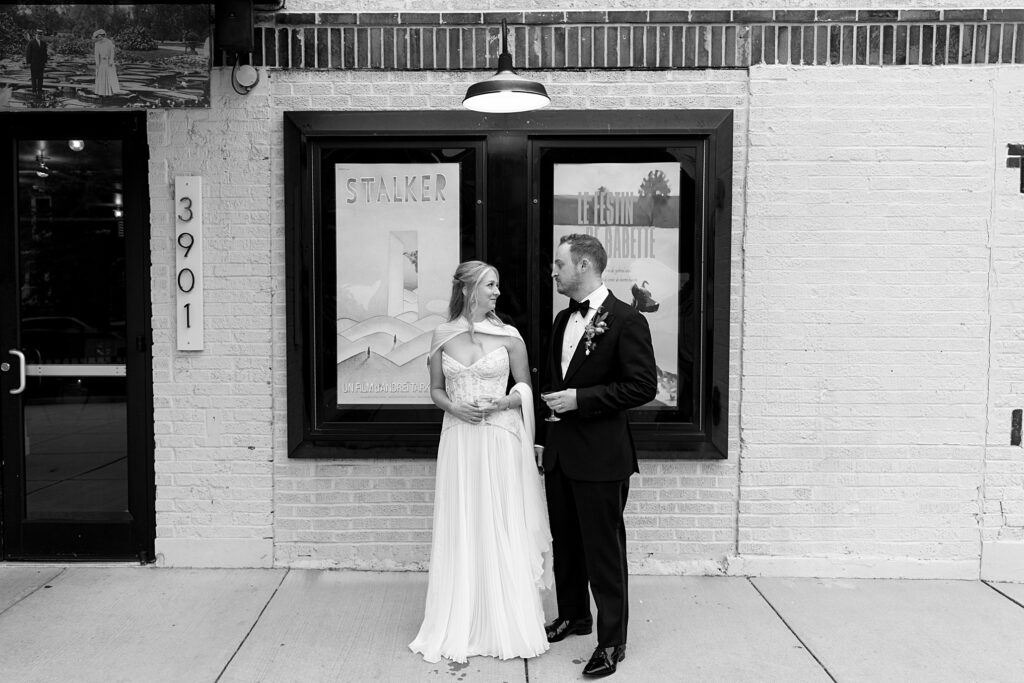 Black and white image of bride and groom looking at each other, with drinks in hand, outside of the Wild Carrot wedding venue in St. Louis, Missouri