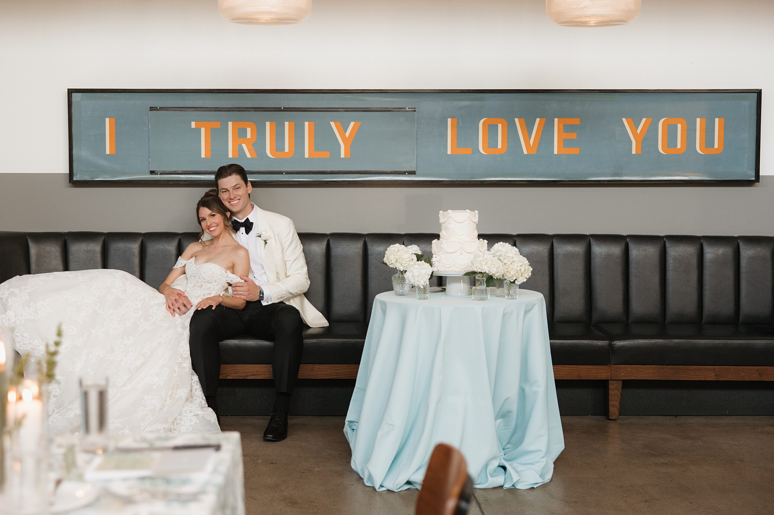 Newlyweds sitting together under a sign that says "I truly love you" during their Olive + Oak wedding